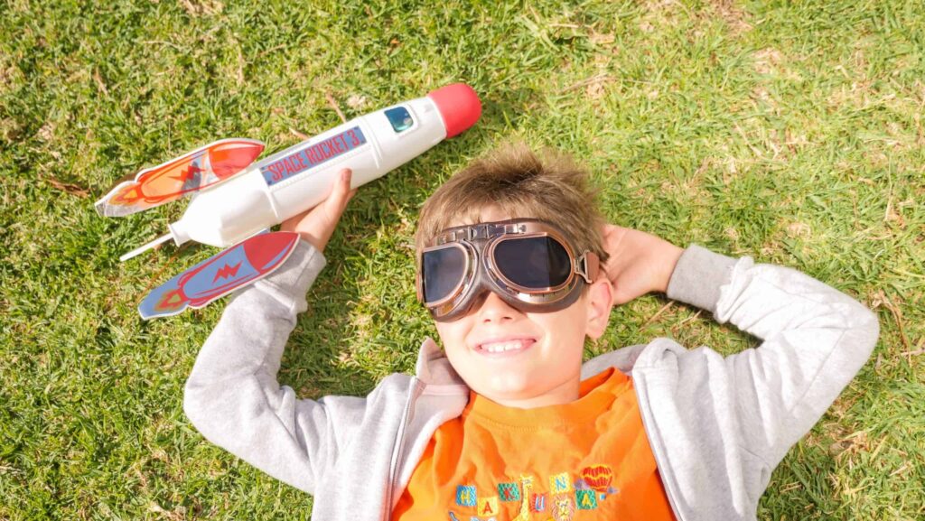 Enfant observant le soleil avec des lunettes d'aviateur et tenant dans la main une fusée